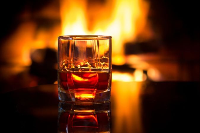 Glass of whisky next to an open fire
