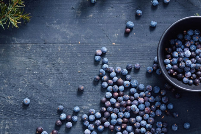 Juniper berries in a black bowl and spread out on a wooden table