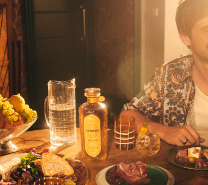 Renais gin founder Alex Watson sat at a table laughing with his bottle of gin.