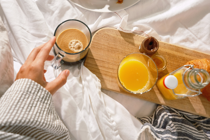 A wooden platter filled with croissants and juice is being enjoyed in bed by a hotel visitor
