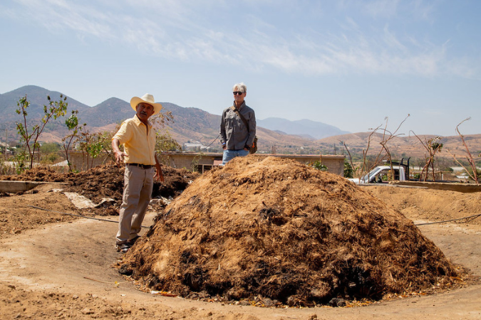 Two men stand by a mount of dry mud