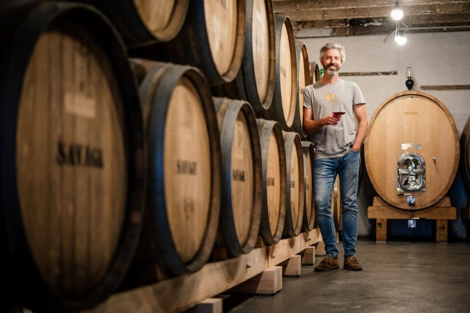 Duncan Savage stands with a glass of wine in the winery cellar