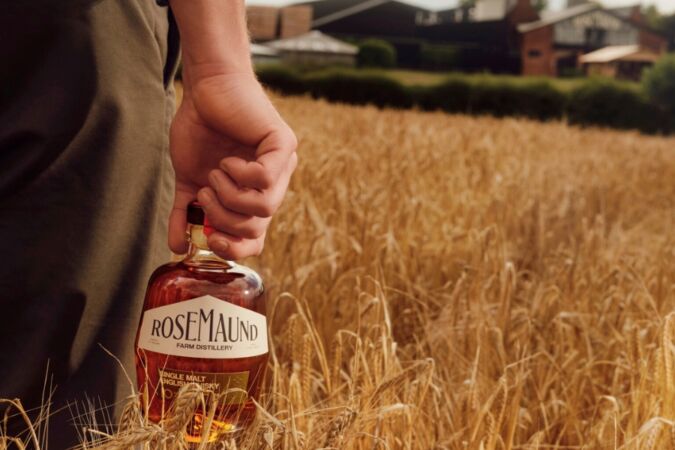 Man holding a bottle of Rosemaund whisky in a field of grain