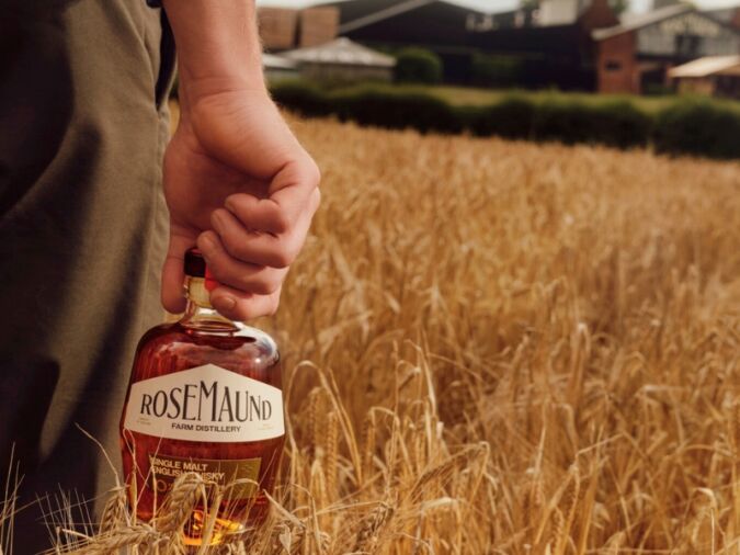 Man holding a bottle of Rosemaund whisky in a field of grain