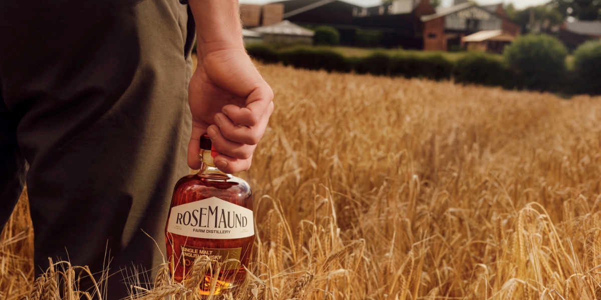 Man holding a bottle of Rosemaund whisky in a field of grain