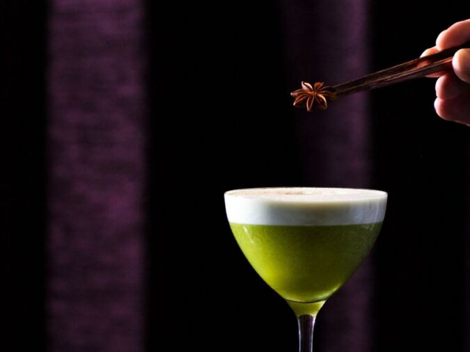 green cocktail with garnish being added by tweezers