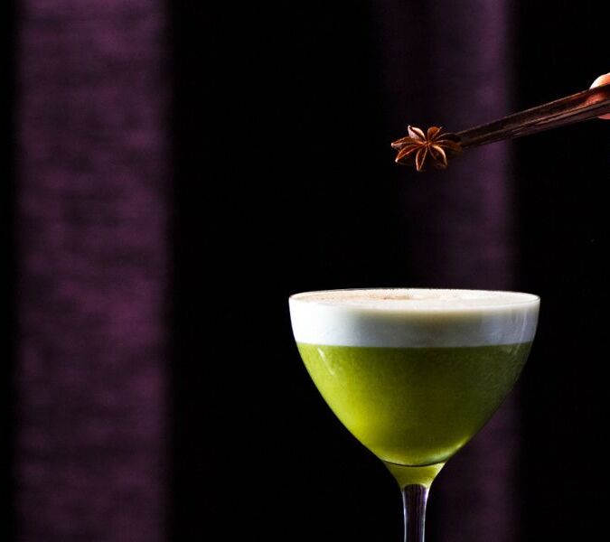 green cocktail with garnish being added by tweezers