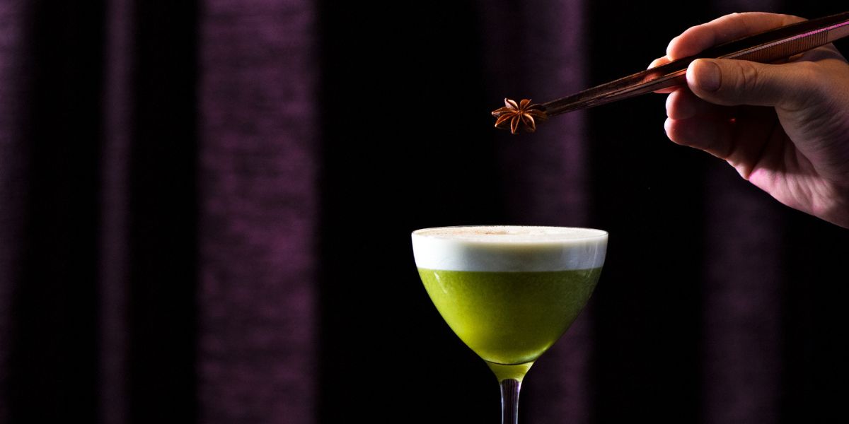 green cocktail with garnish being added by tweezers