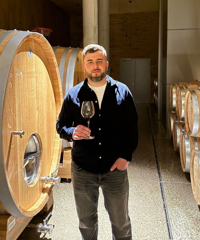 Giorgi Shiukashvili holding glass of wine by barrels in Koncho & Co winery