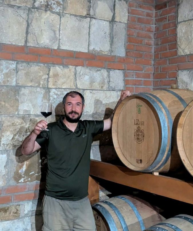 Winemaker Sandro Chalatashvili holds wine glass by barrels in the Lionidzis Zvari winery