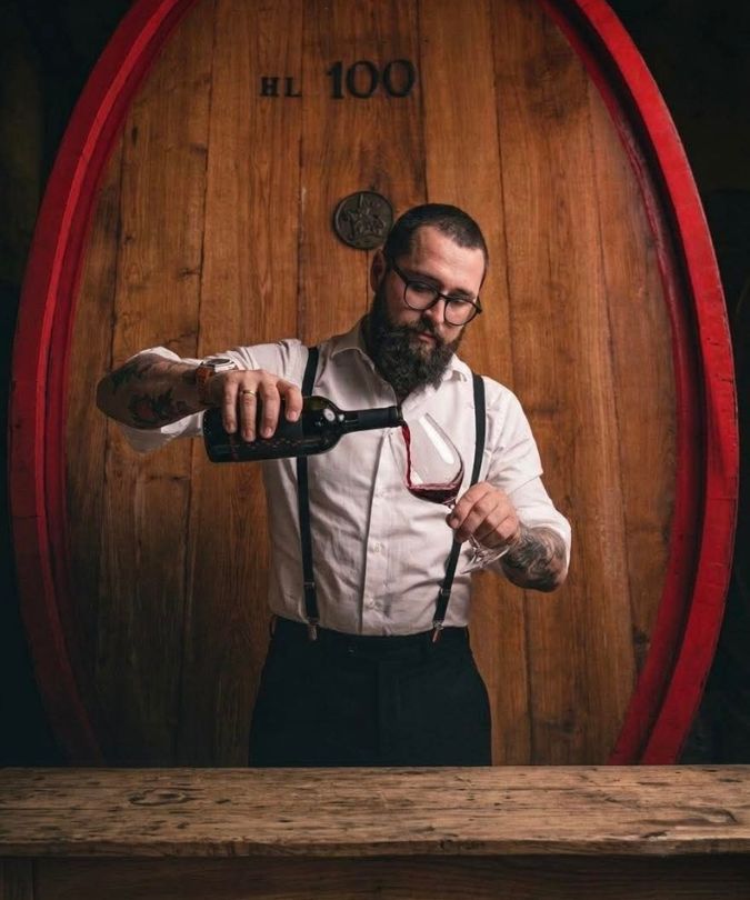 Barbales Marani winemaker Tornike Matitashvili pours red wine in front of large barrel